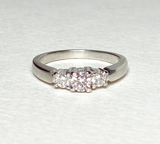 Platinum three-stone ring with a light pink diamond center and two white diamonds.