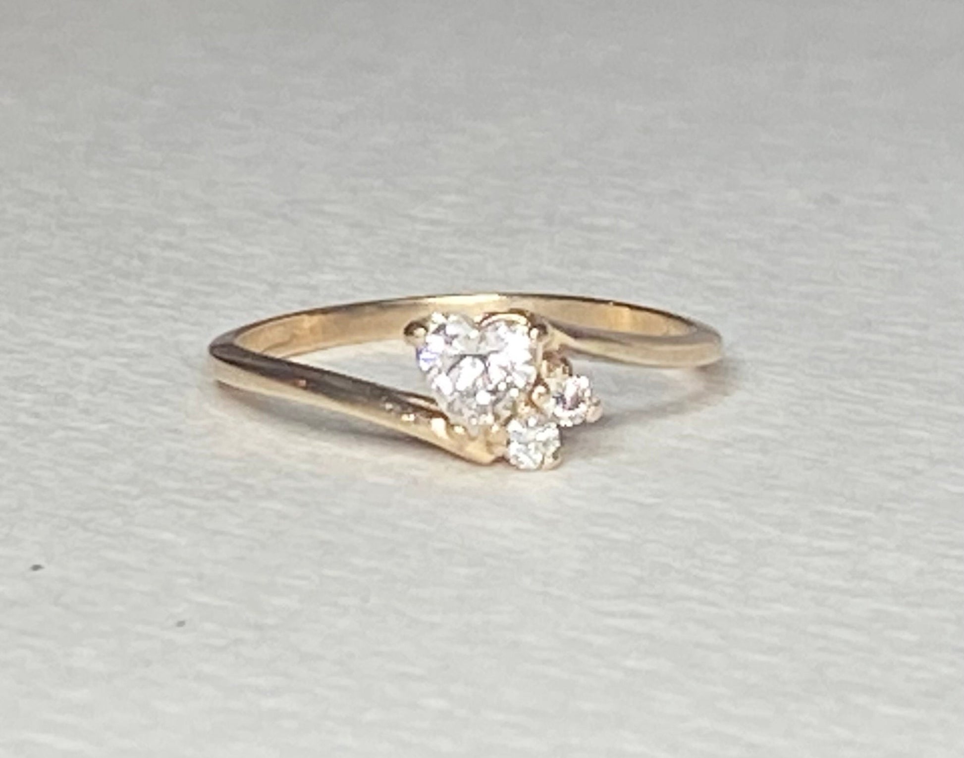 A 14k gold ring with a heart-shaped diamond and two smaller accent diamonds.