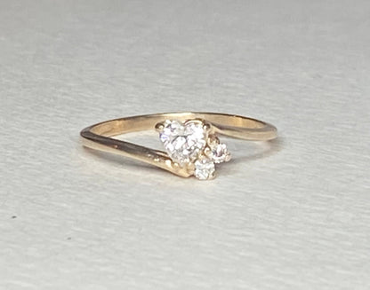A 14k gold ring with a heart-shaped diamond and two smaller accent diamonds.