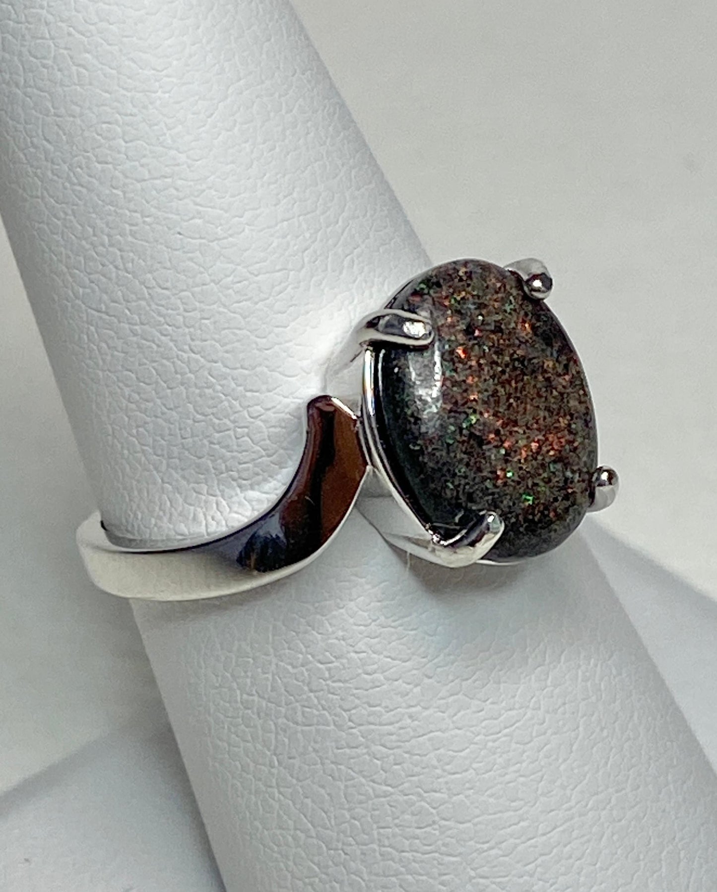 Sterling silver ring with an oval pinfire boulder opal on a white textured surface.