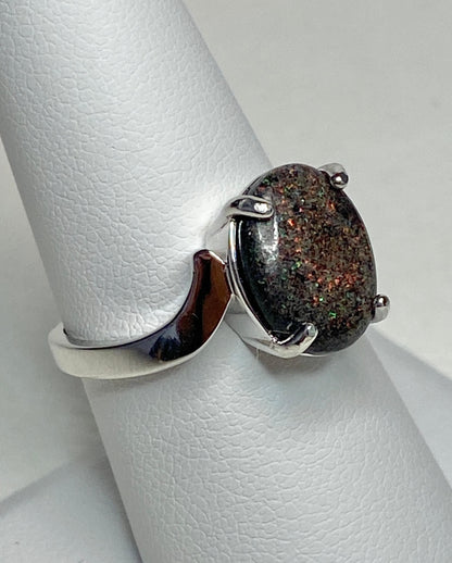 Sterling silver ring with an oval pinfire boulder opal on a white textured surface.