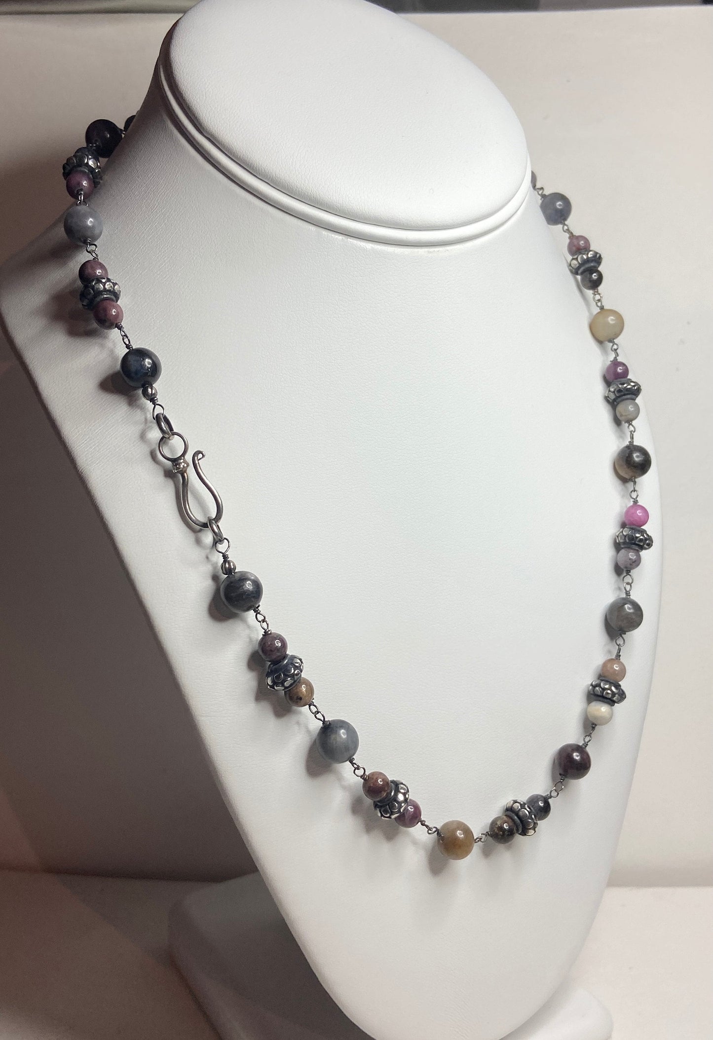 A multi-color natural sapphire beaded necklace with sterling silver accents on a white display.