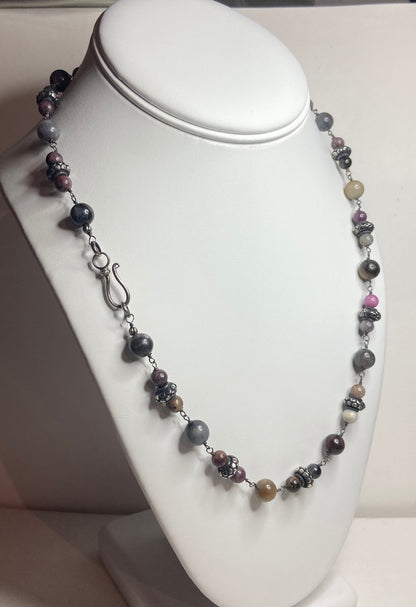 A multi-color natural sapphire beaded necklace with sterling silver accents on a white display.