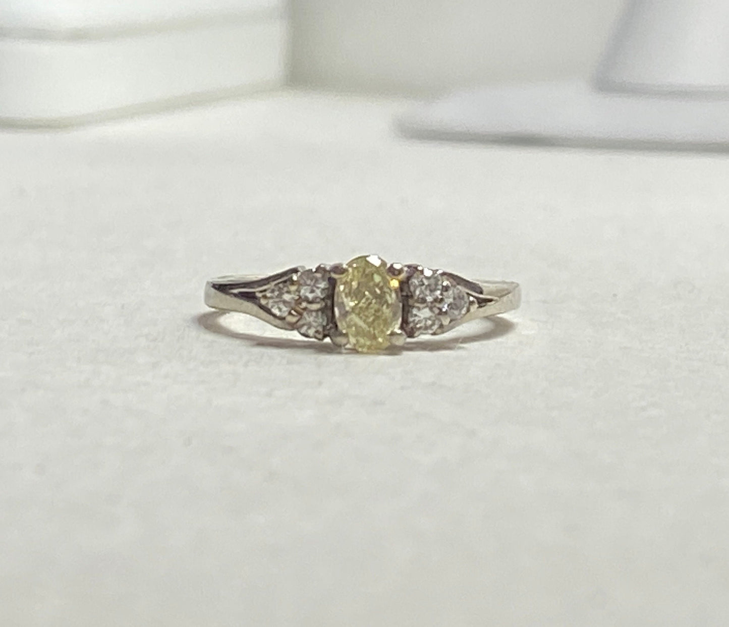 Oval fancy light yellow diamond ring with white diamonds in 14k gold.