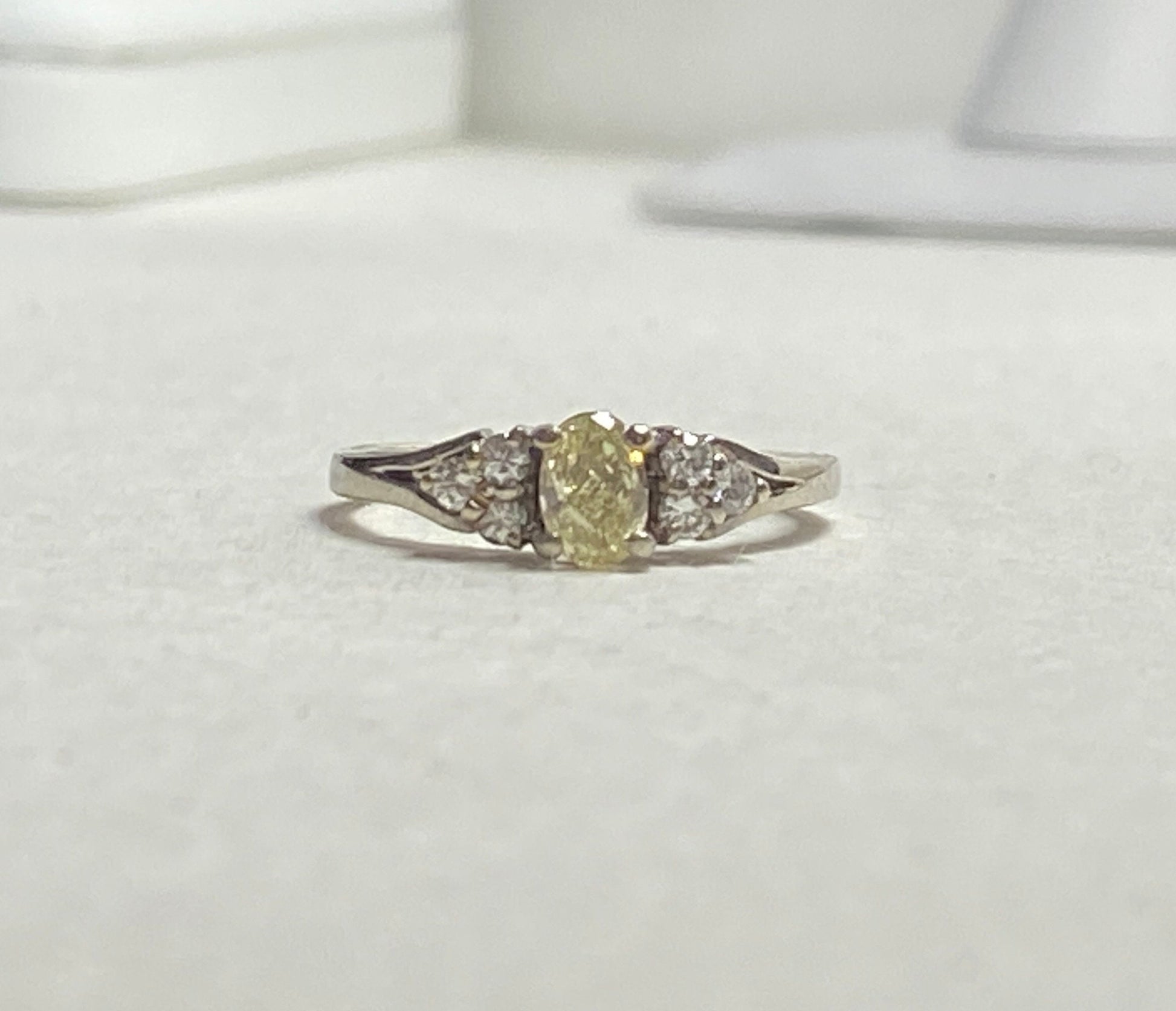 Oval fancy light yellow diamond ring with white diamonds in 14k gold.