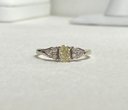 Oval fancy light yellow diamond ring with white diamonds in 14k gold.
