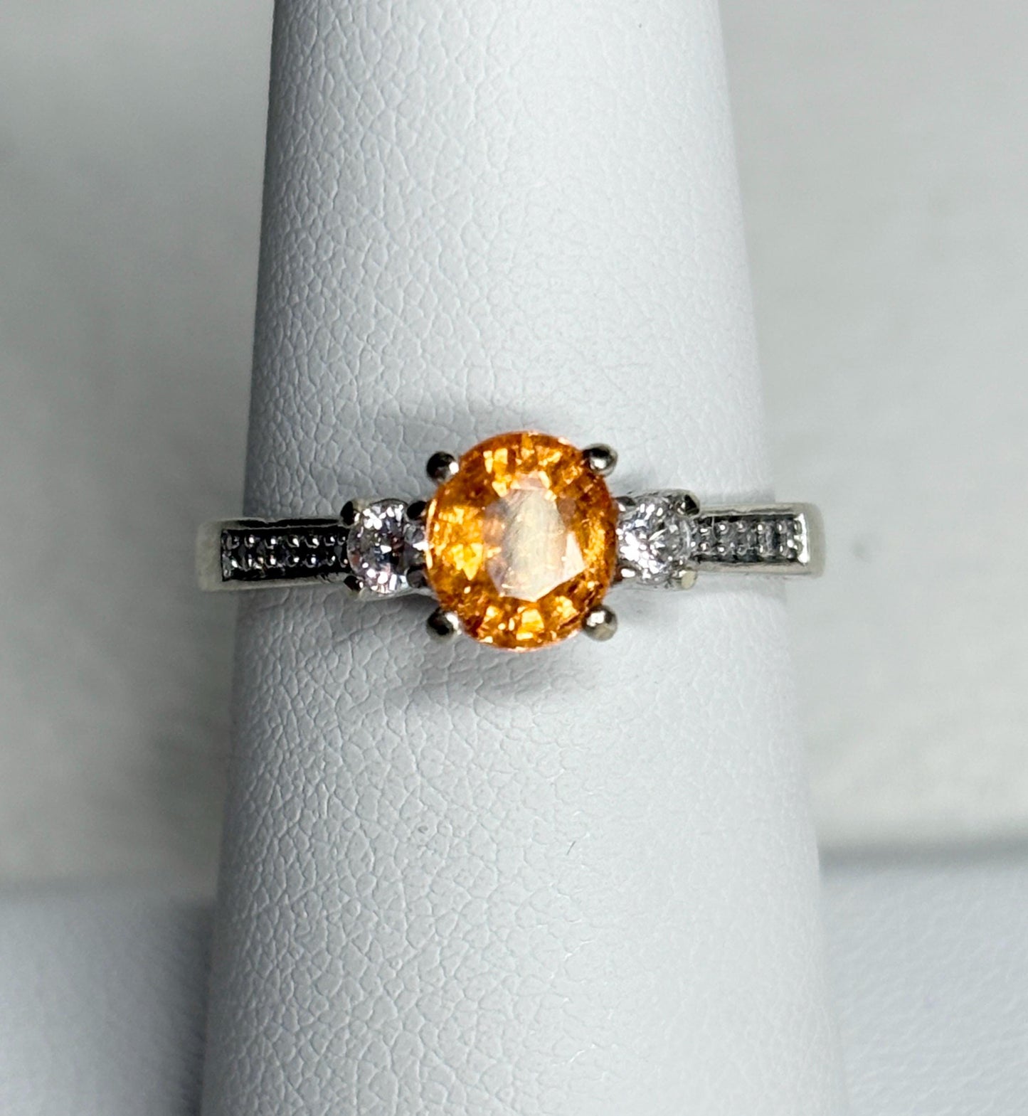 A 10k white gold ring with a central orange spessartite garnet and accent diamonds.