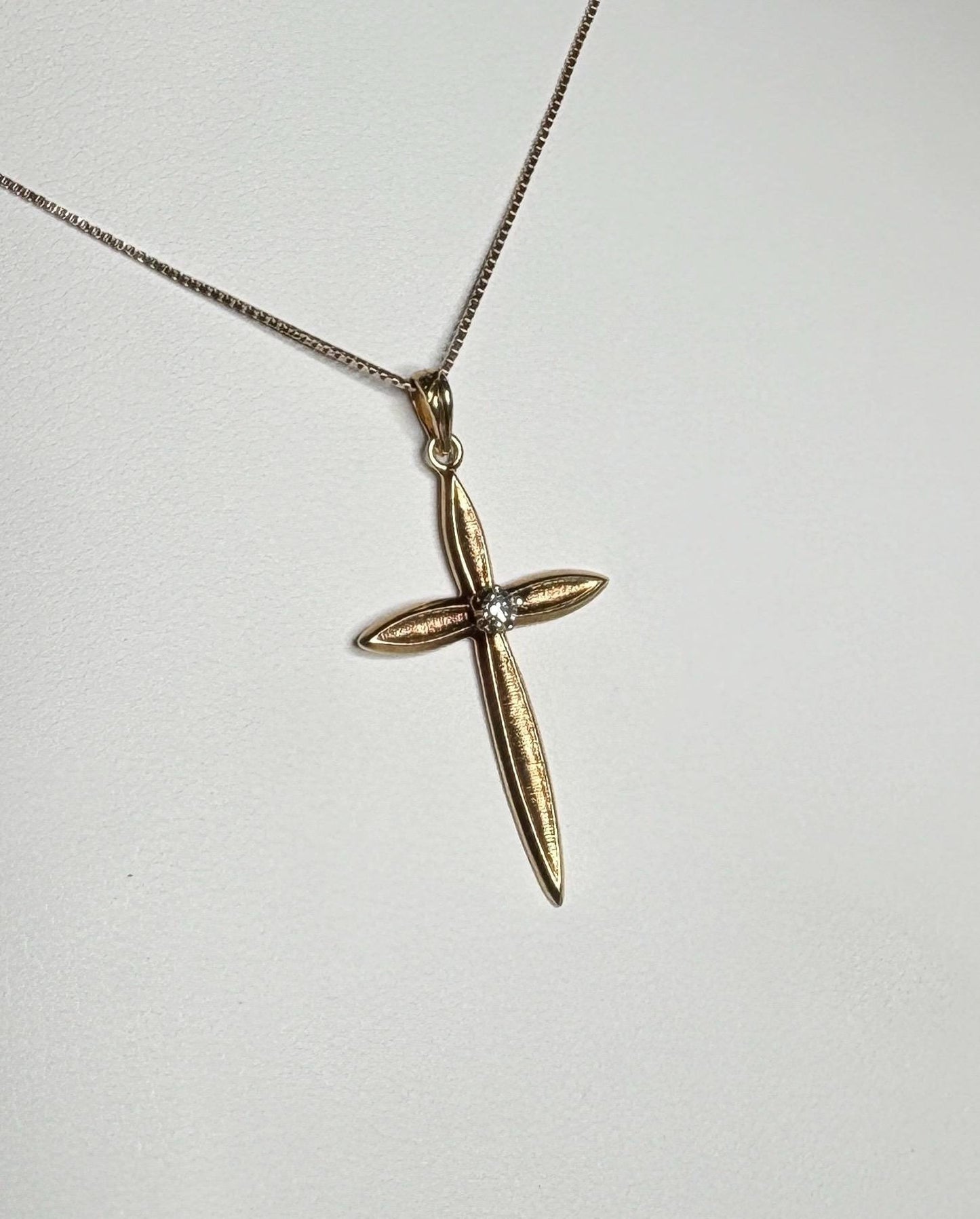 A gold cross pendant with a diamond on a gold box chain necklace.