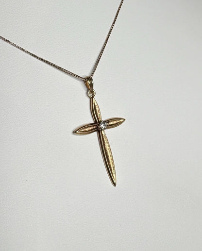 A gold cross pendant with a diamond on a gold box chain necklace.