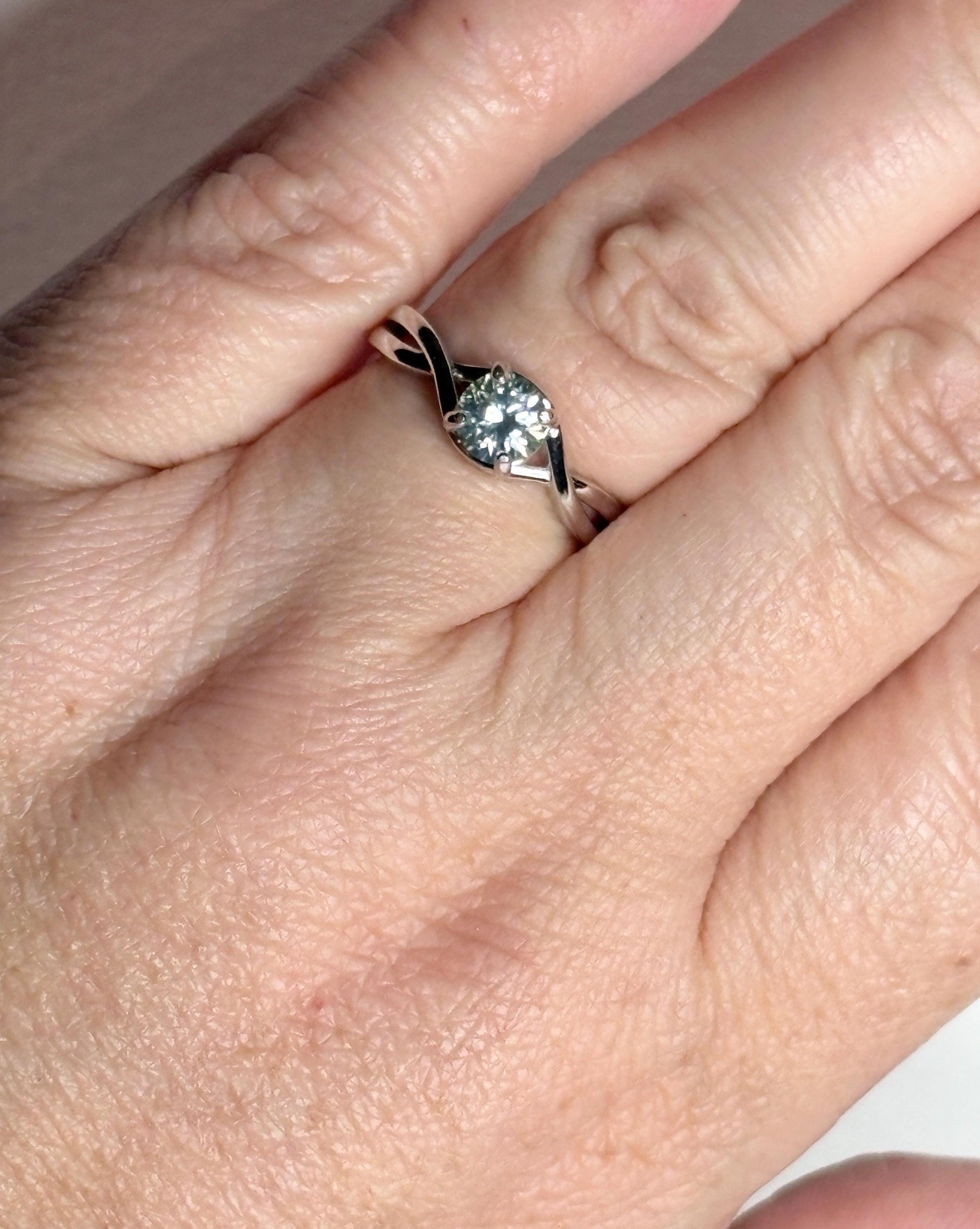 Sterling silver bypass ring with a light greenish-blue moissanite solitaire.
