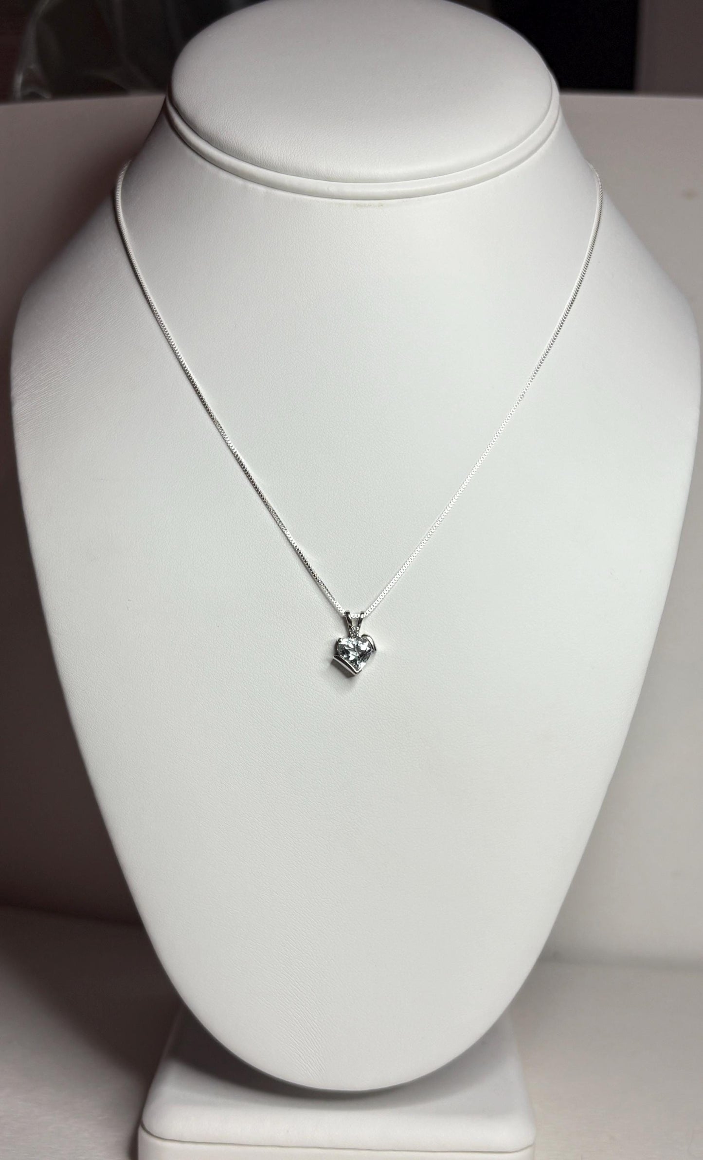 A white gold heart pendant with an aquamarine and diamond on a silver chain.