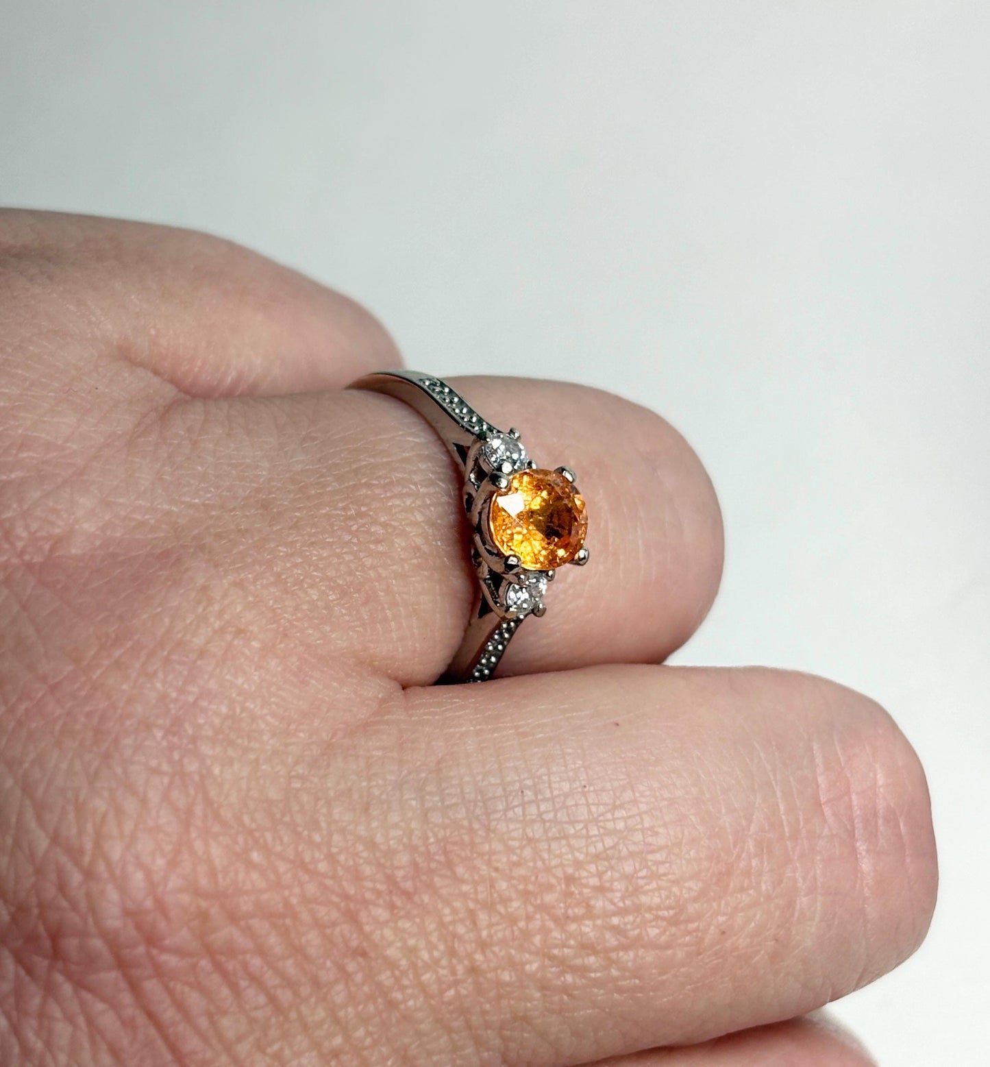 A 10k white gold ring with an oval orange spessartite garnet and two diamonds.