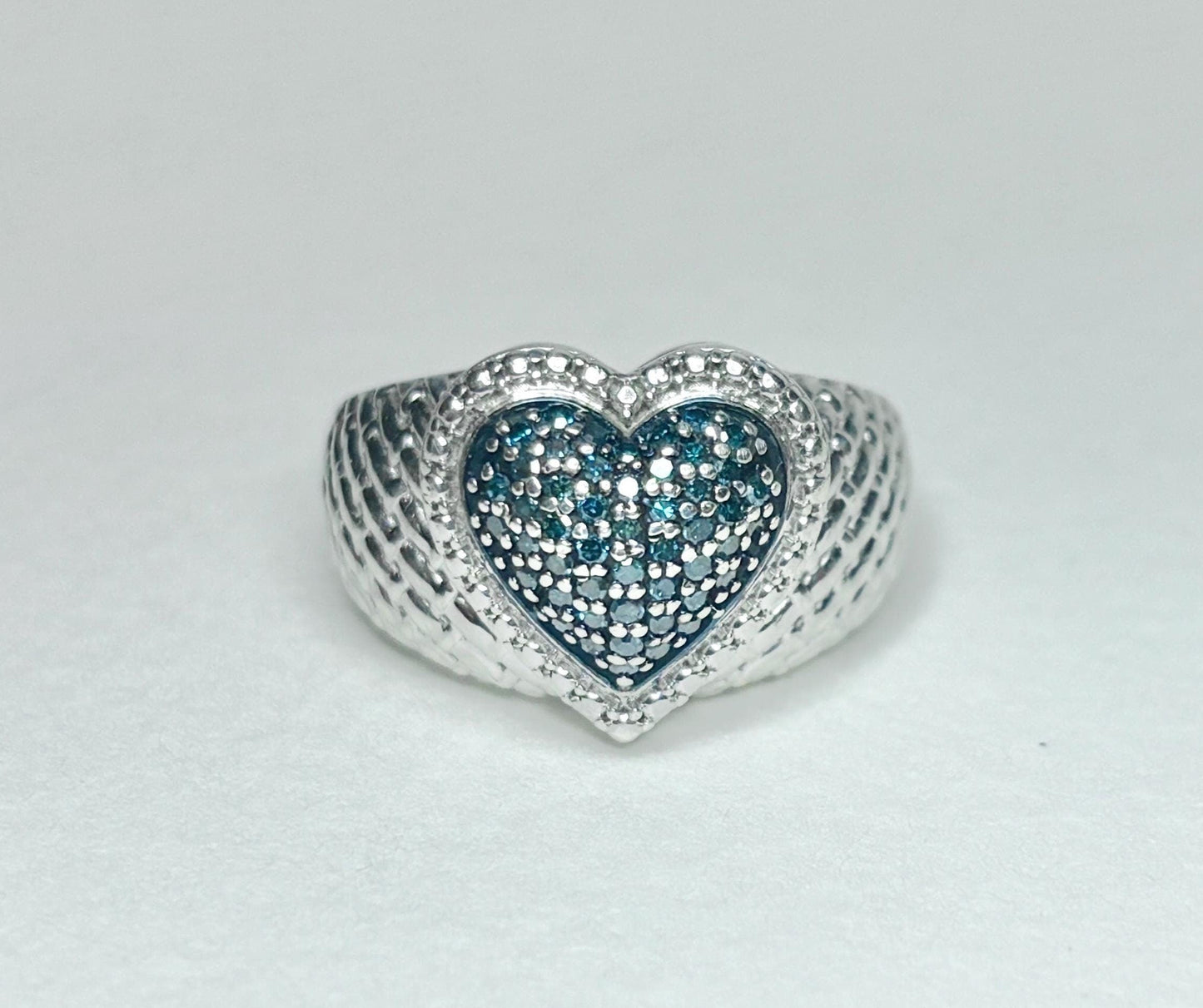 Sterling silver ring with a quilted band and a heart-shaped center filled with blue diamonds.