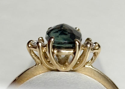 A 14k yellow gold ring with a teal oval Montana sapphire and two small diamonds.
