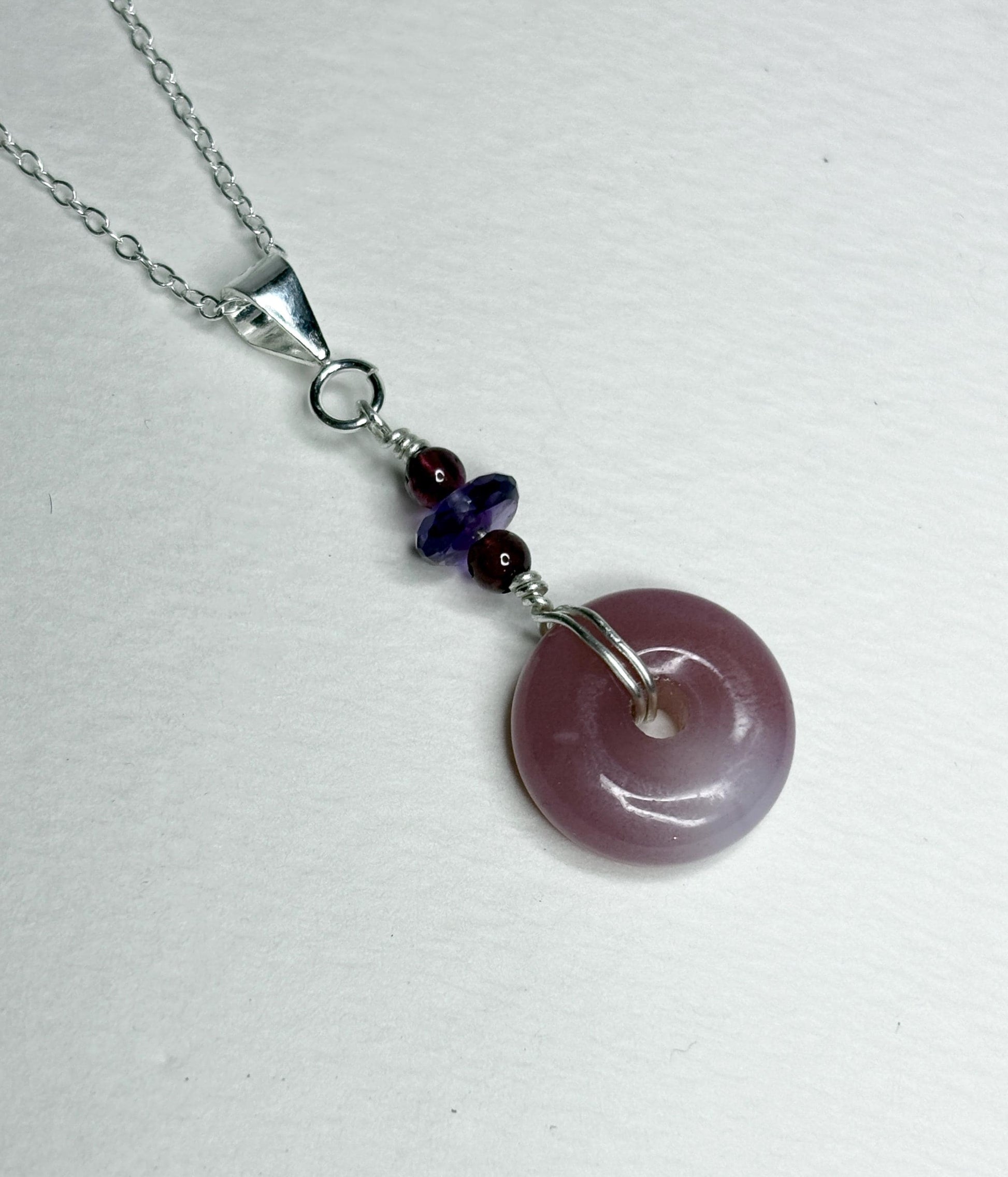 Sterling silver pendant necklace with a mauve-pink agate donut and amethyst and garnet beads.