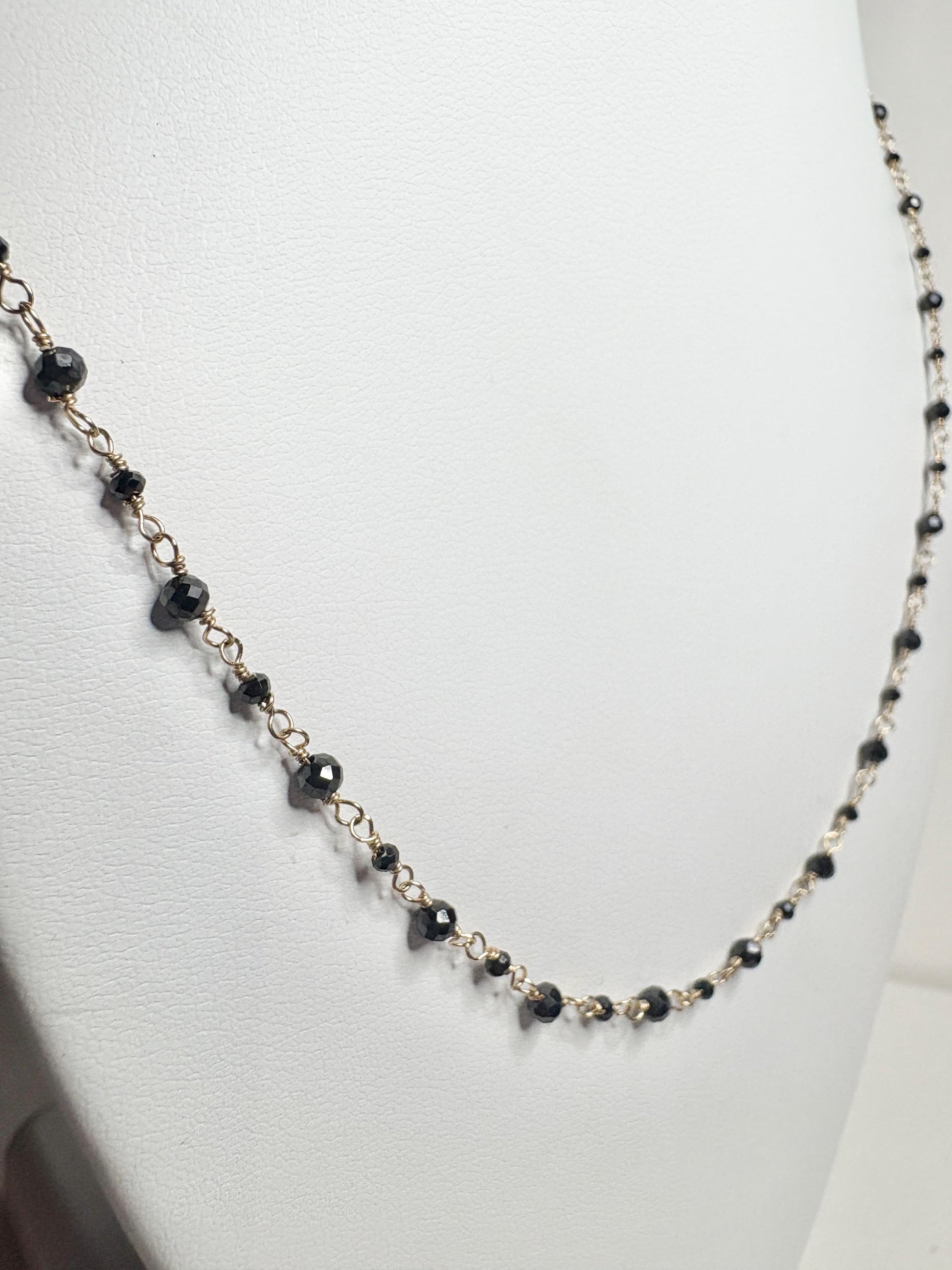 A delicate 14k gold necklace with small, faceted black diamonds.