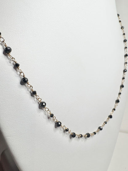 A delicate 14k gold necklace with small, faceted black diamonds.