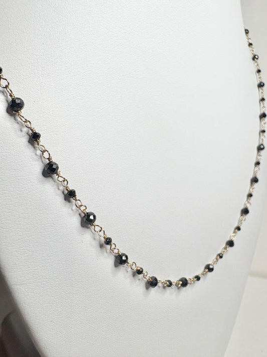 A delicate 14k gold necklace with small, faceted black diamonds.