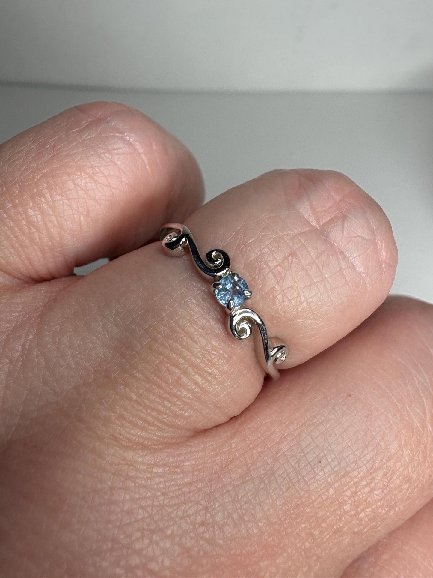 Sterling silver ring with a light blue sapphire and swirl band.
