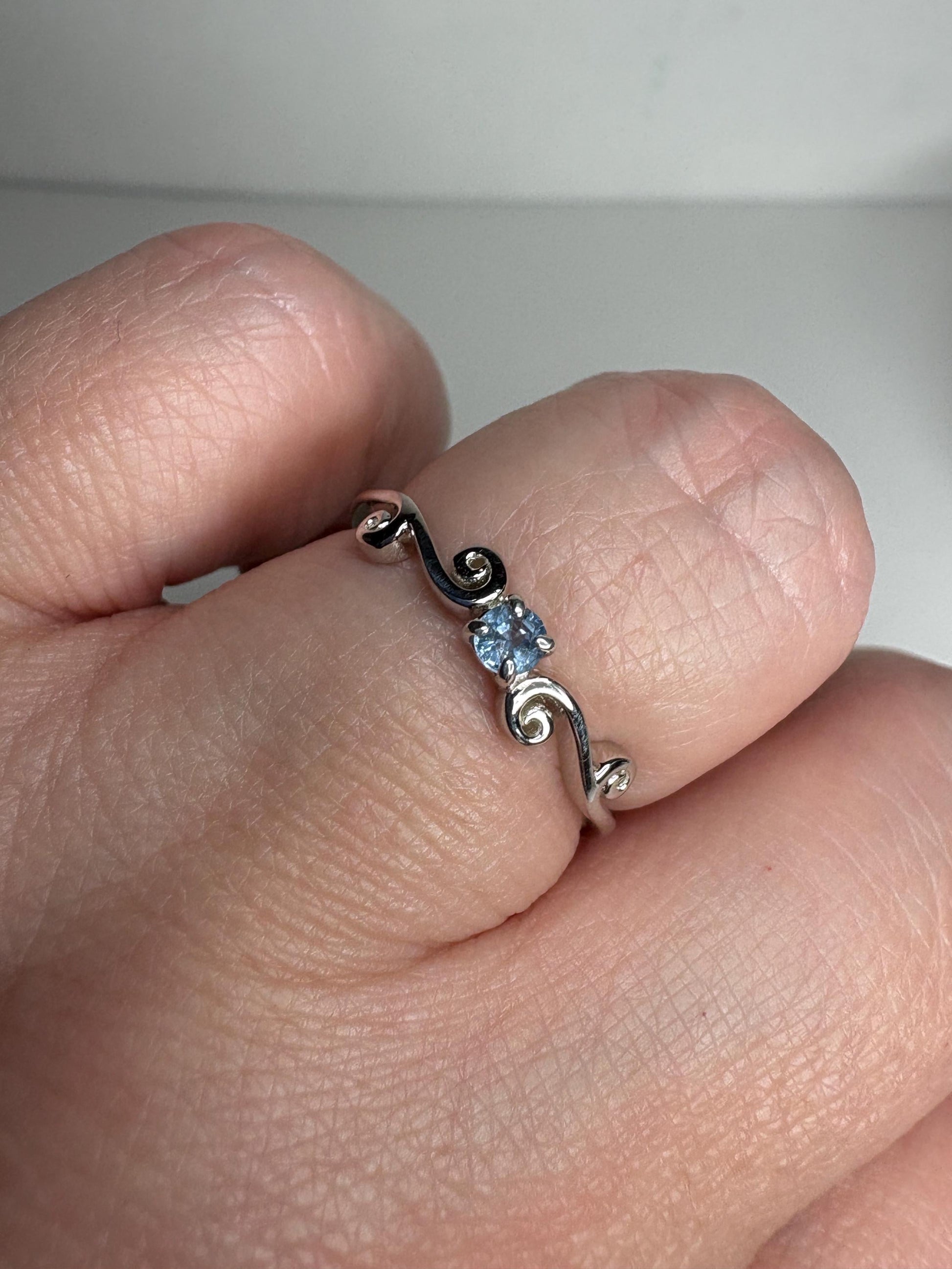 Sterling silver ring with a light blue sapphire and swirl band.