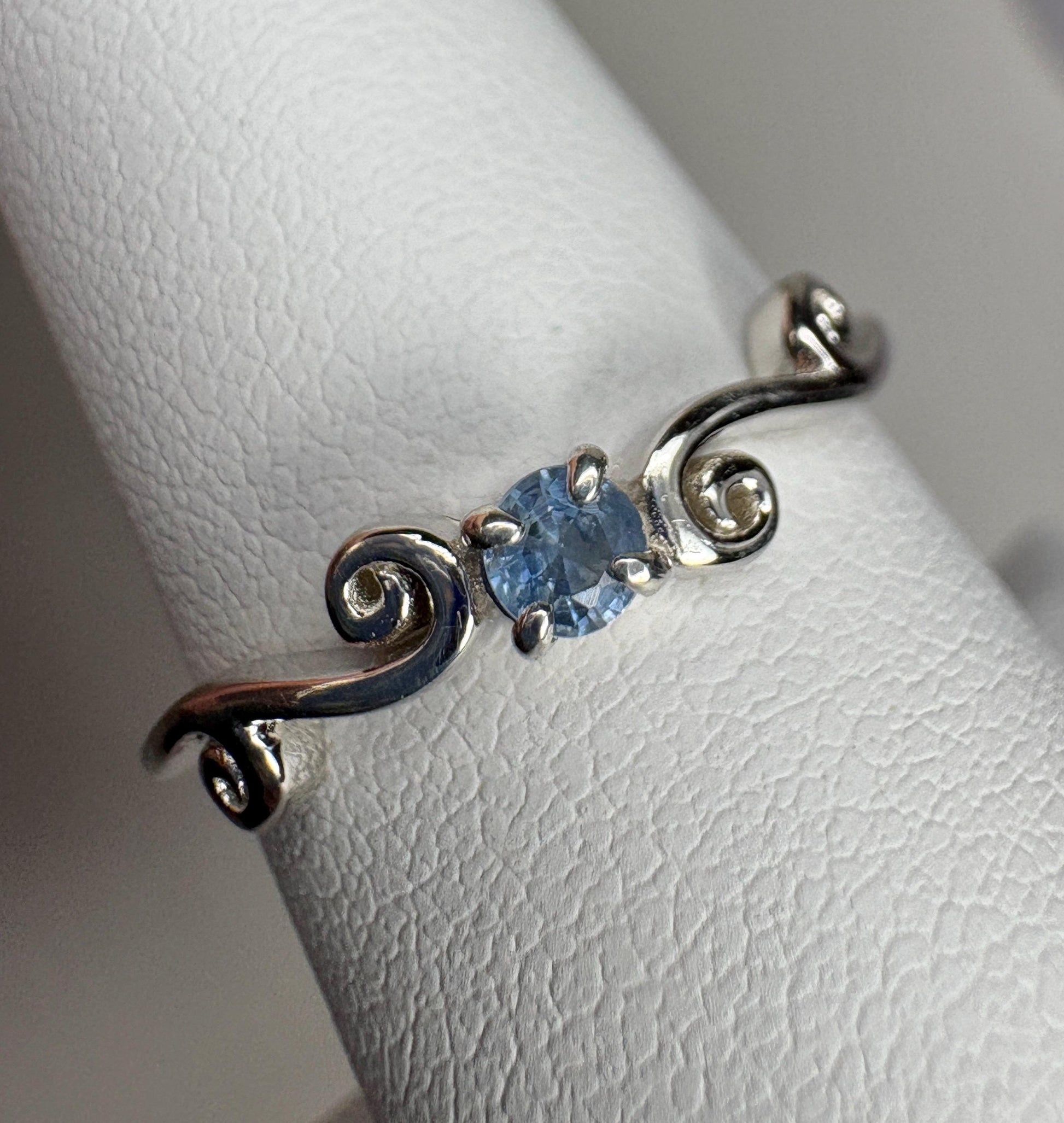 Sterling silver ring with a light blue sapphire and swirl band.