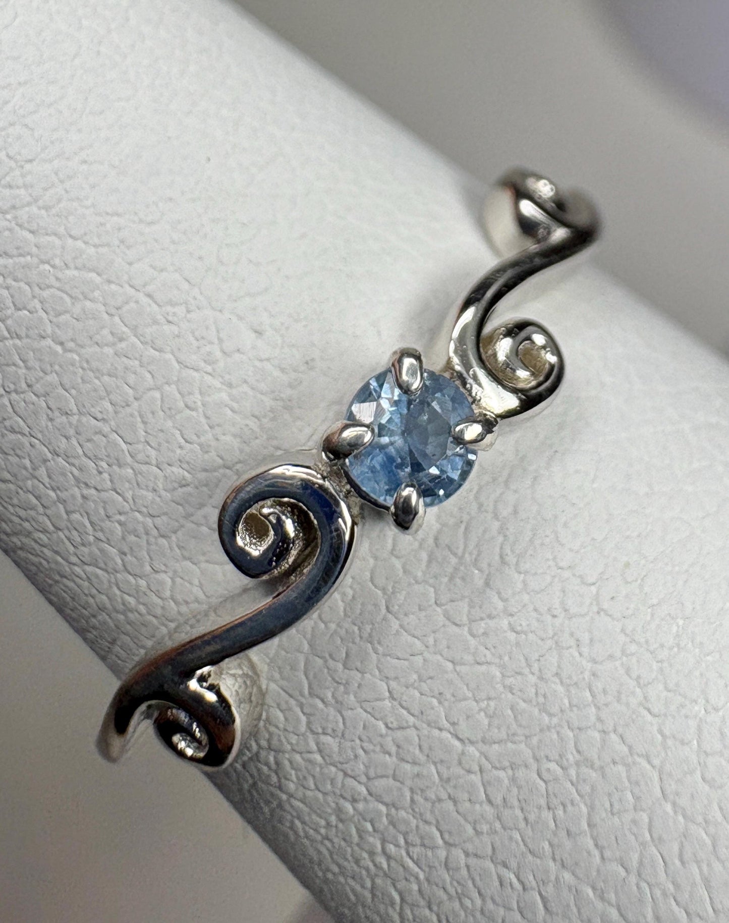 Sterling silver ring with a light blue sapphire and swirl band.