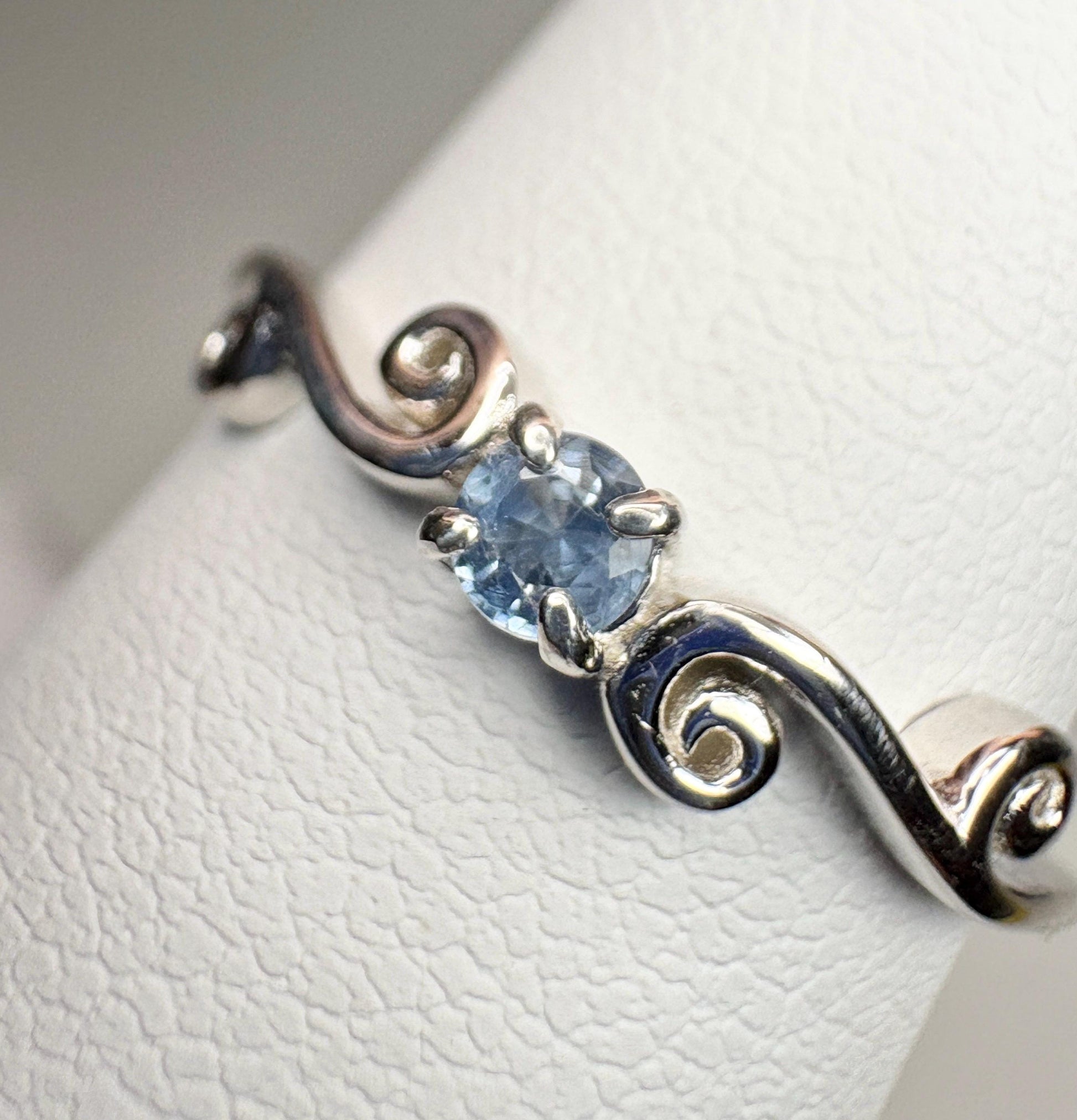 Sterling silver ring with a light blue sapphire and swirl band.