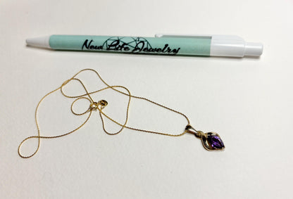 A gold necklace with an amethyst pendant and a pen with "New Life Jewelry" logo.