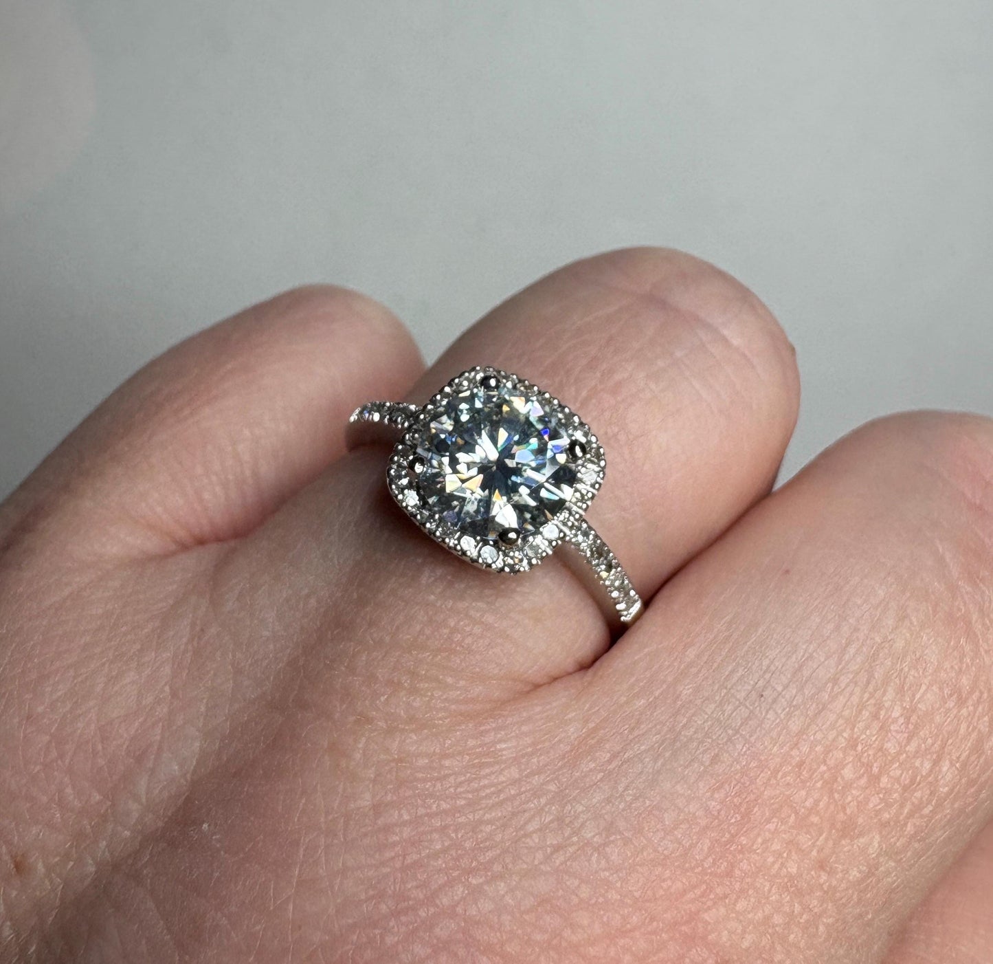 A white gold ring with a large moissanite center stone surrounded by small diamonds.