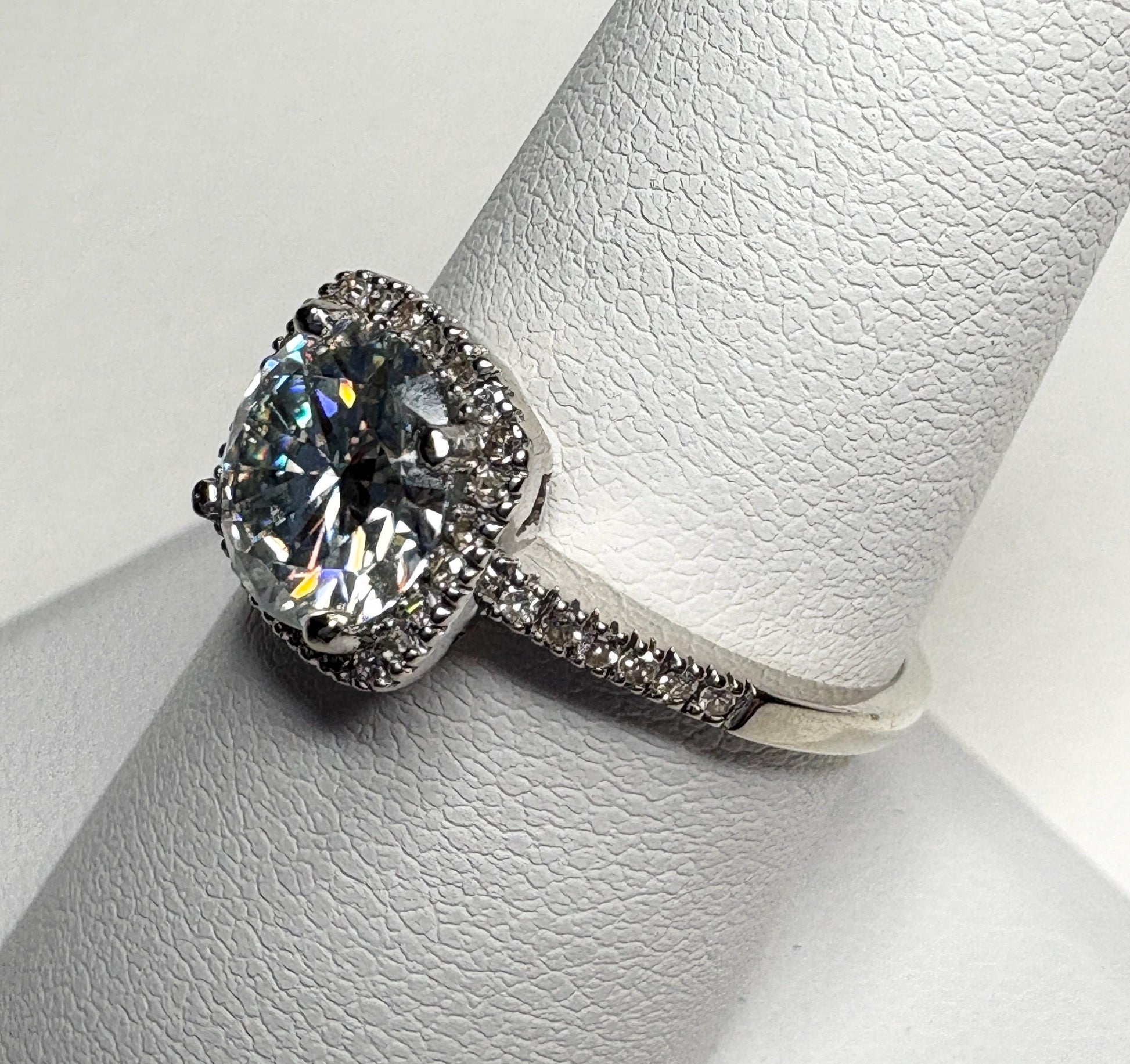 A white gold ring with a large moissanite center stone surrounded by small diamonds.
