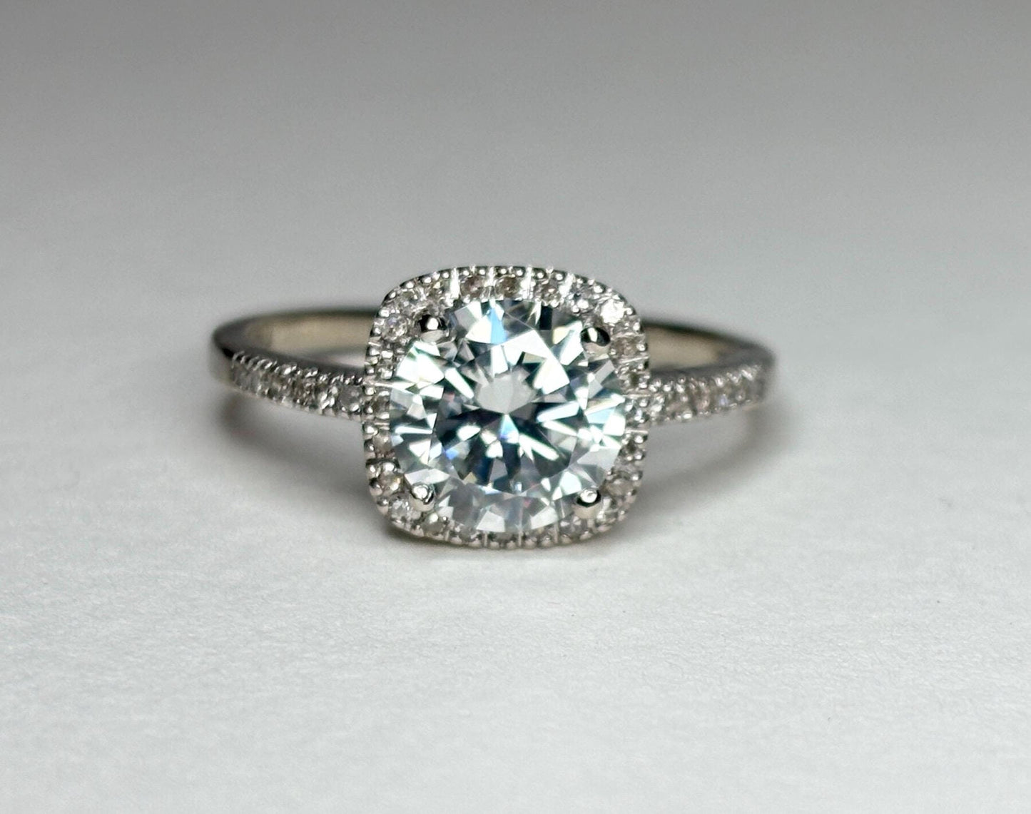 A white gold ring with a large moissanite center stone surrounded by small diamonds.