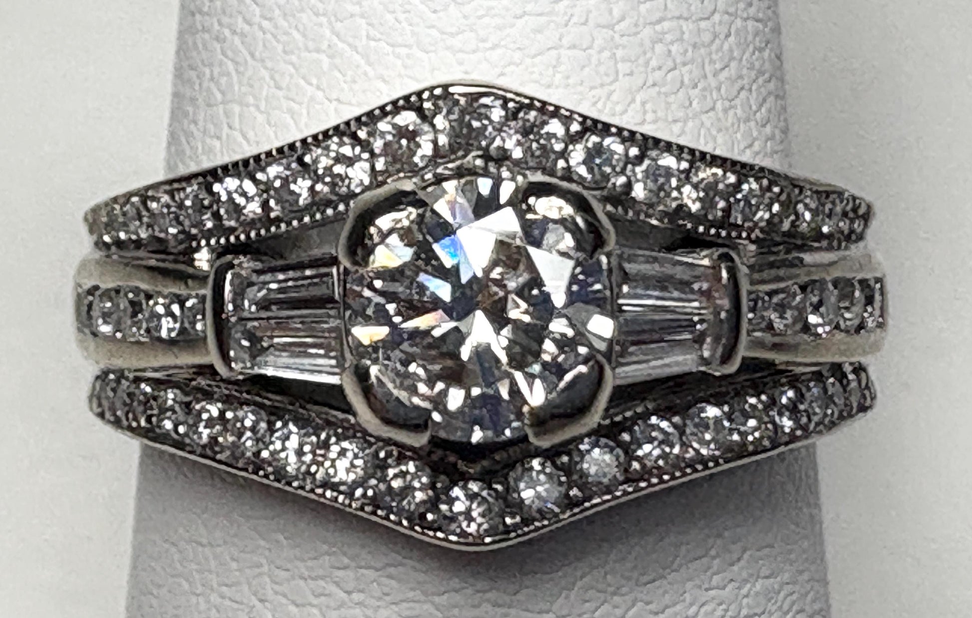 A 14k white gold engagement ring with a central diamond and baguette and round accent diamonds.