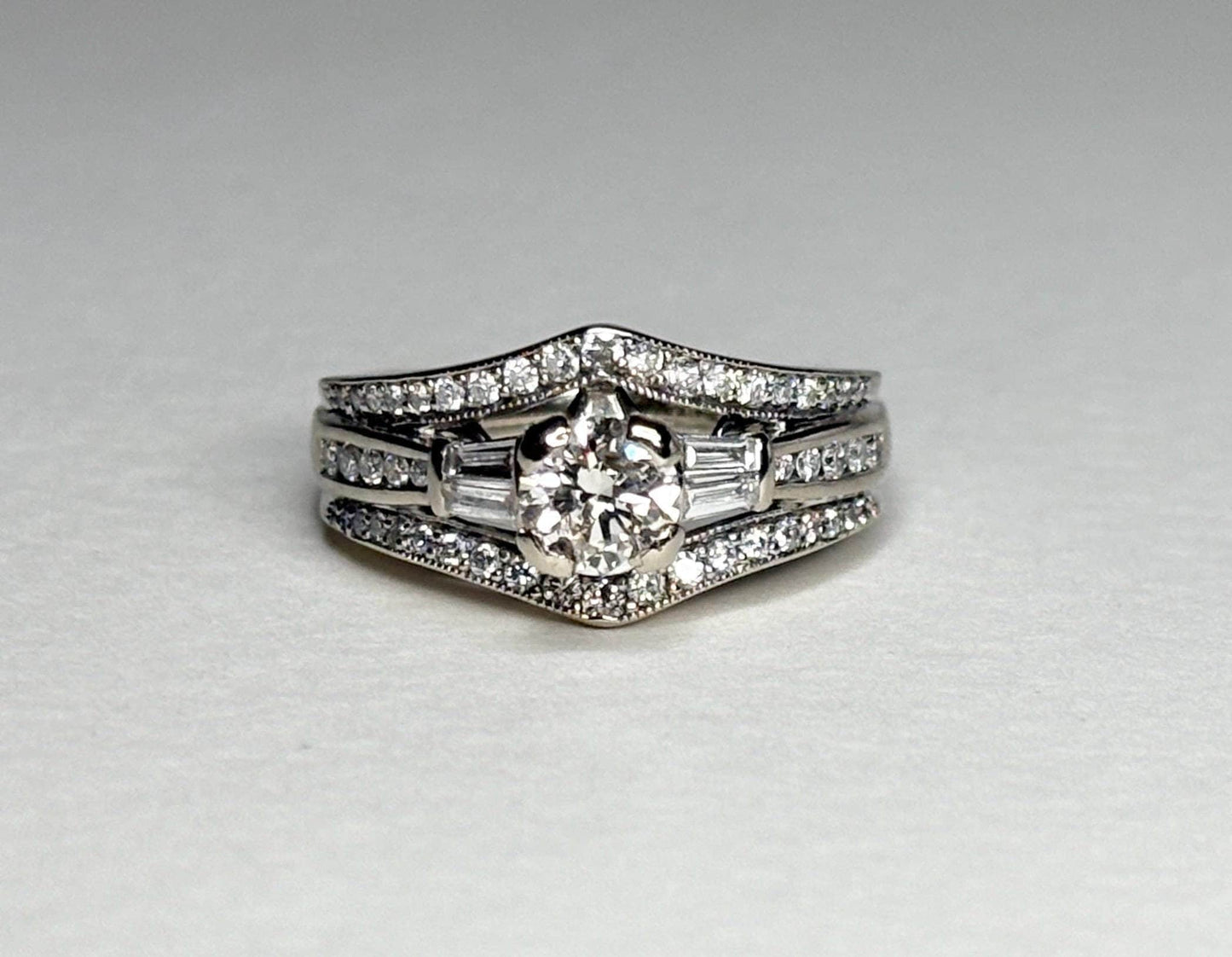 A 14k white gold engagement ring with a round center diamond and baguette side stones, surrounded by smaller diamonds.