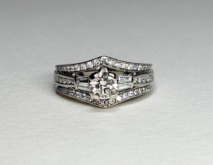 A 14k white gold engagement ring with a round center diamond and baguette side stones, surrounded by smaller diamonds.