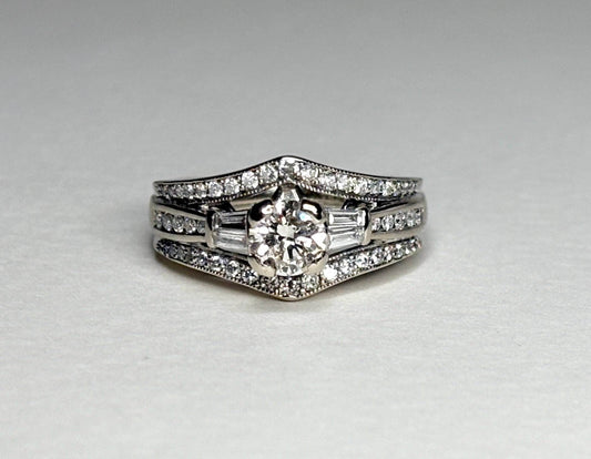 A 14k white gold engagement ring with a round center diamond and baguette side stones, surrounded by smaller diamonds.