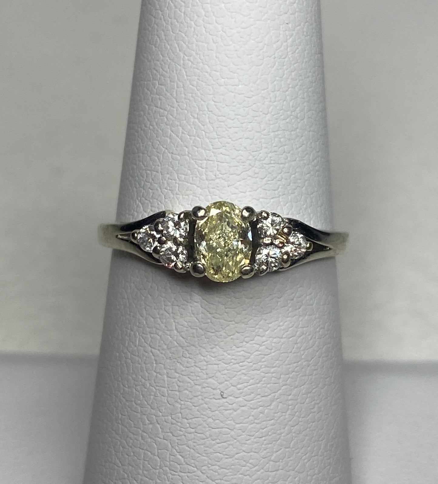 A 14k gold ring with a light yellow oval diamond and white side diamonds.