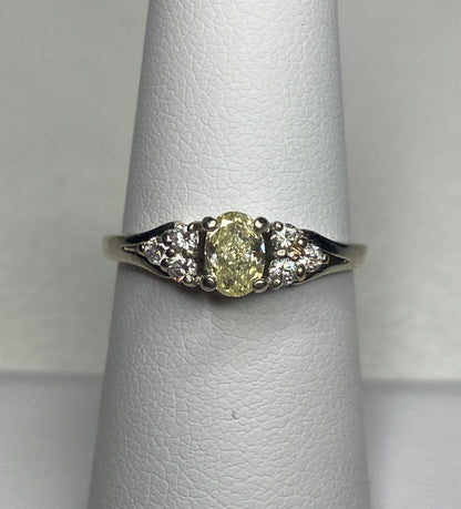 A 14k gold ring with a light yellow oval diamond and white side diamonds.