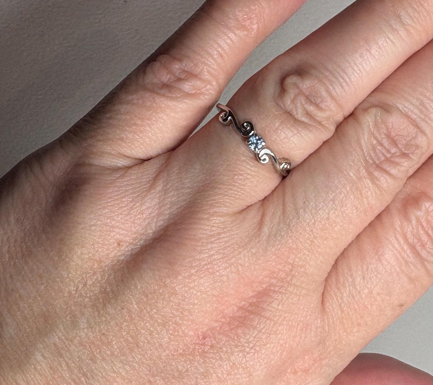 Sterling silver ring with a natural light blue sapphire and swirl band.