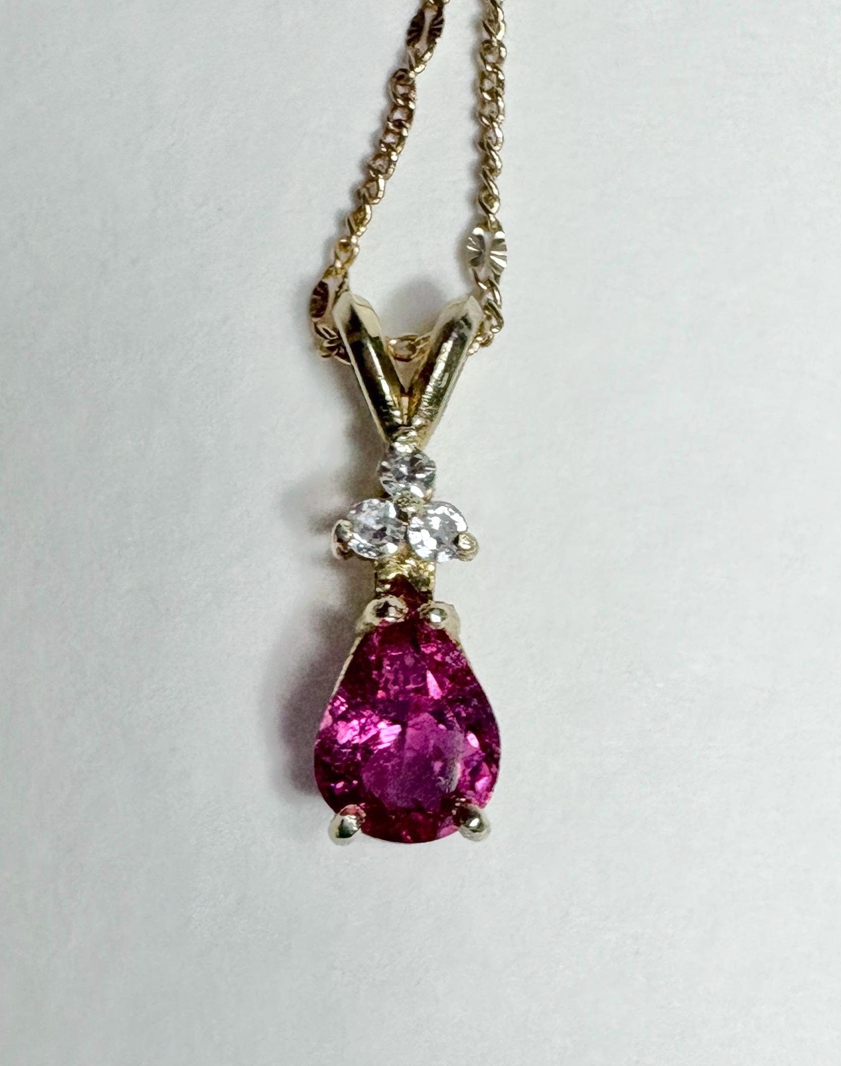A pear-shaped rubellite tourmaline pendant with diamonds on a gold chain.