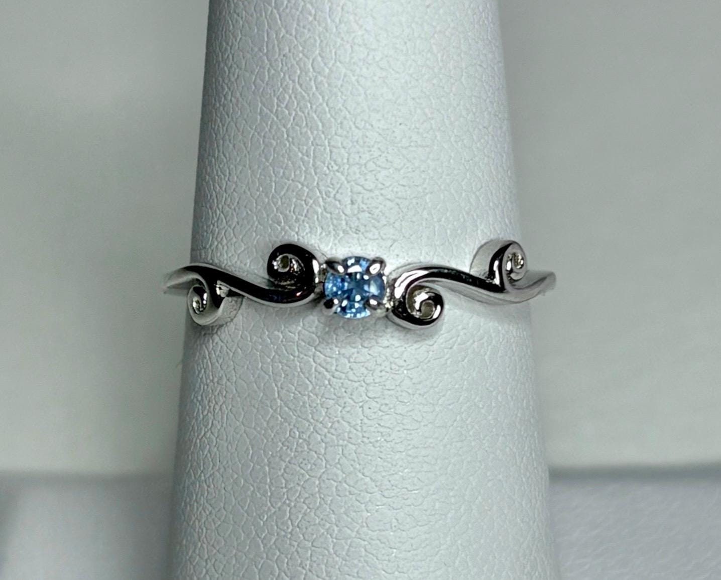 Sterling silver ring with a light blue sapphire and swirl band.