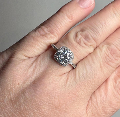 A white gold ring with a large moissanite center stone surrounded by small diamonds.