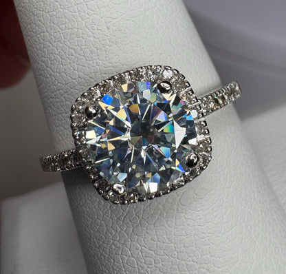 A white gold ring with a large moissanite center stone surrounded by small diamonds.