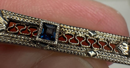 Antique bar brooch with a blue gemstone and intricate gold detailing.