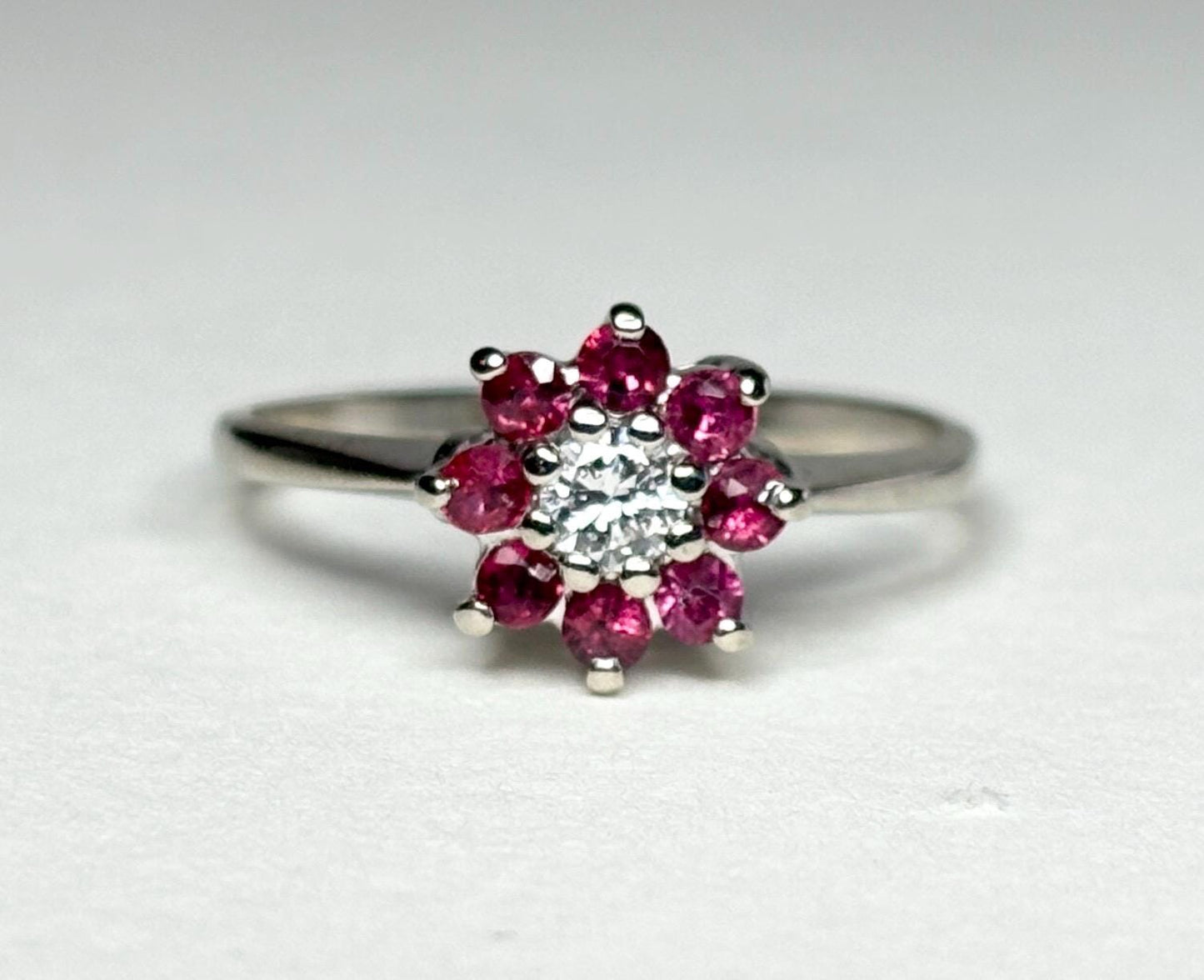 14k white gold ring with a diamond center and ruby daisy halo.