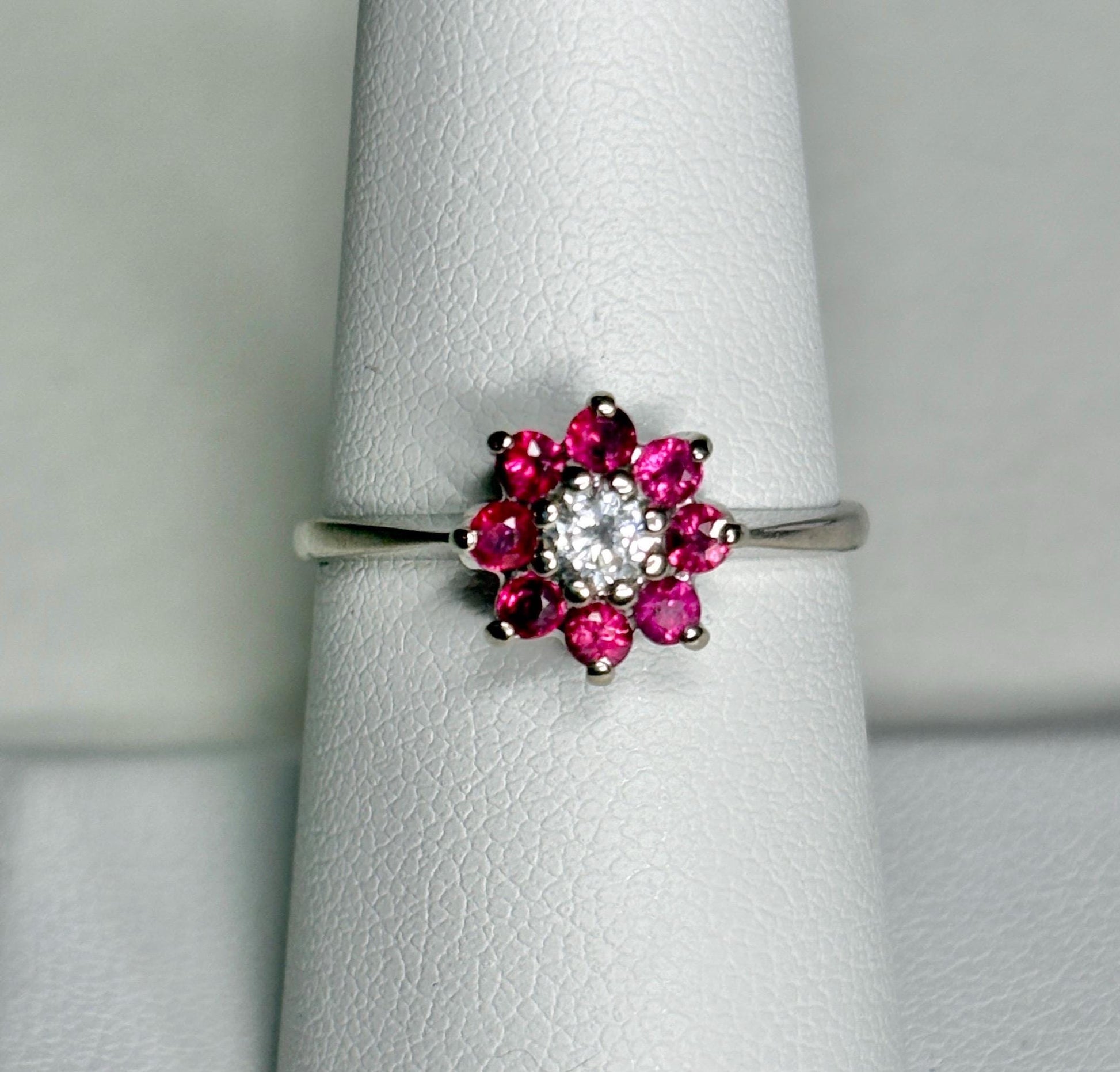 A 14k white gold ring with a diamond center and a ruby daisy halo.