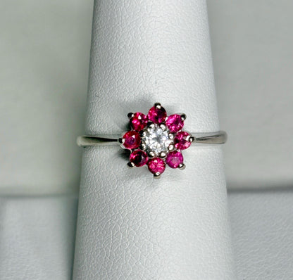 A 14k white gold ring with a diamond center and a ruby daisy halo.