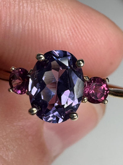 Ring with oval color change synthetic sapphire and two round umbalite garnets in gold.