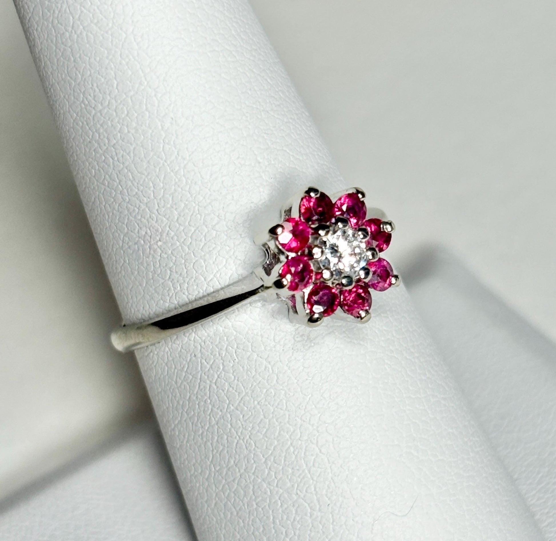 A 14k white gold ring with a diamond center and ruby daisy halo.
