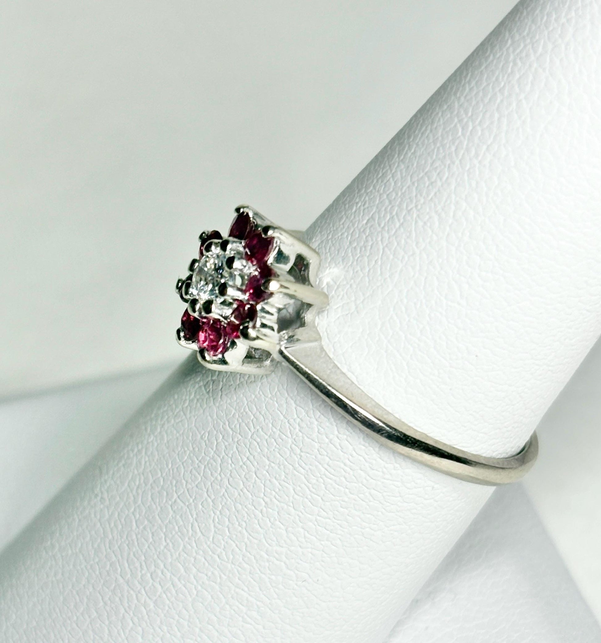 A 14k white gold ring with a diamond center surrounded by rubies in a daisy halo design.