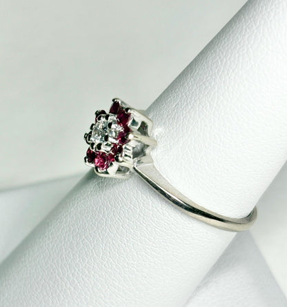 A 14k white gold ring with a diamond center surrounded by rubies in a daisy halo design.